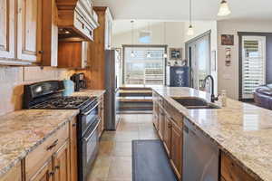 Kitchen with stainless steel appliances, light stone countertops, pendant lighting, wood finish cabinetry, and lofted ceiling