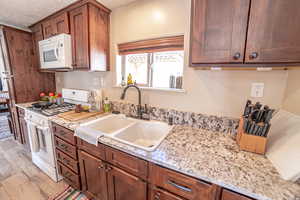 Kitchen with white appliances, a textured ceiling, light stone countertops, light wood-type flooring, and wood finish cabinetry