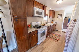 Kitchen featuring white appliances, light wood finished floors, a textured ceiling, light stone countertops, and wood finish cabinets
