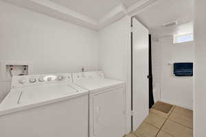 Laundry area featuring light tile patterned floors, washing machine and clothes dryer, and a textured ceiling