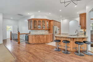 Kitchen with a peninsula, glass fronted cabinets, a kitchen breakfast bar, light stone counters, and light wood-style floors