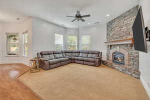 Living area with a ceiling fan, a stone fireplace, recessed lighting, and wood finished floors