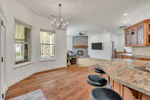 Kitchen featuring hanging lights, glass insert cabinets, light stone counters, a fireplace, and a ceiling fan