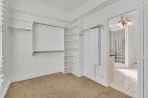 Walk in closet with light carpet and suspended lighting