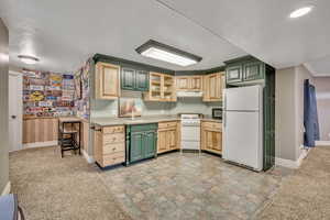 Kitchen featuring light colored carpet, white appliances, light countertops, green cabinetry, and stone finish flooring
