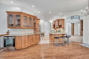 Kitchen featuring glass fronted cabinets, light stone counters, backsplash, wine cooler, and recessed lighting