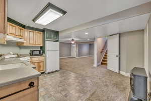 Kitchen featuring light wood finish cabinets, white appliances, light colored carpet, ceiling fan, and open floor plan