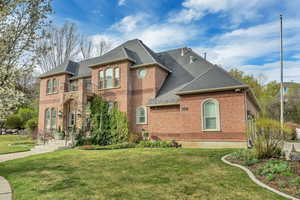 French country style house featuring roof with shingles, brick siding, a front lawn, and a balcony