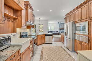 Kitchen featuring open floor plan, stainless steel appliances, a stone fireplace, a warming drawer, and inlaid floor details