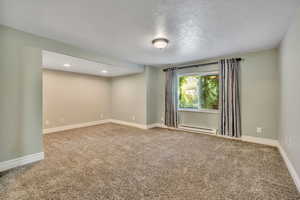 Carpeted empty room featuring a baseboard heating unit and a textured ceiling