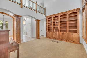 Unfurnished living room with light carpet, a high ceiling, arched walkways, hanging lights, and decorative columns