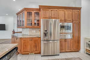 Kitchen with stainless steel appliances, glass fronted cabinets, light stone countertops, wood finish cabinetry, and light tile patterned floors