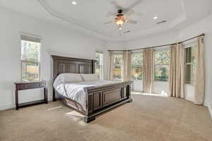Bedroom featuring light carpet, multiple windows, a ceiling fan, a raised ceiling, and crown molding