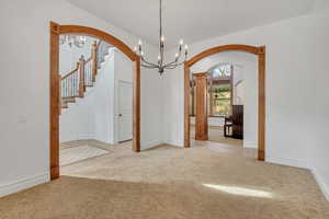 Unfurnished room featuring light carpet, hanging lights, arched walkways, and decorative columns