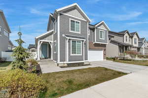 View of front facade with board and batten siding, driveway, brick siding, an attached garage, and a residential view