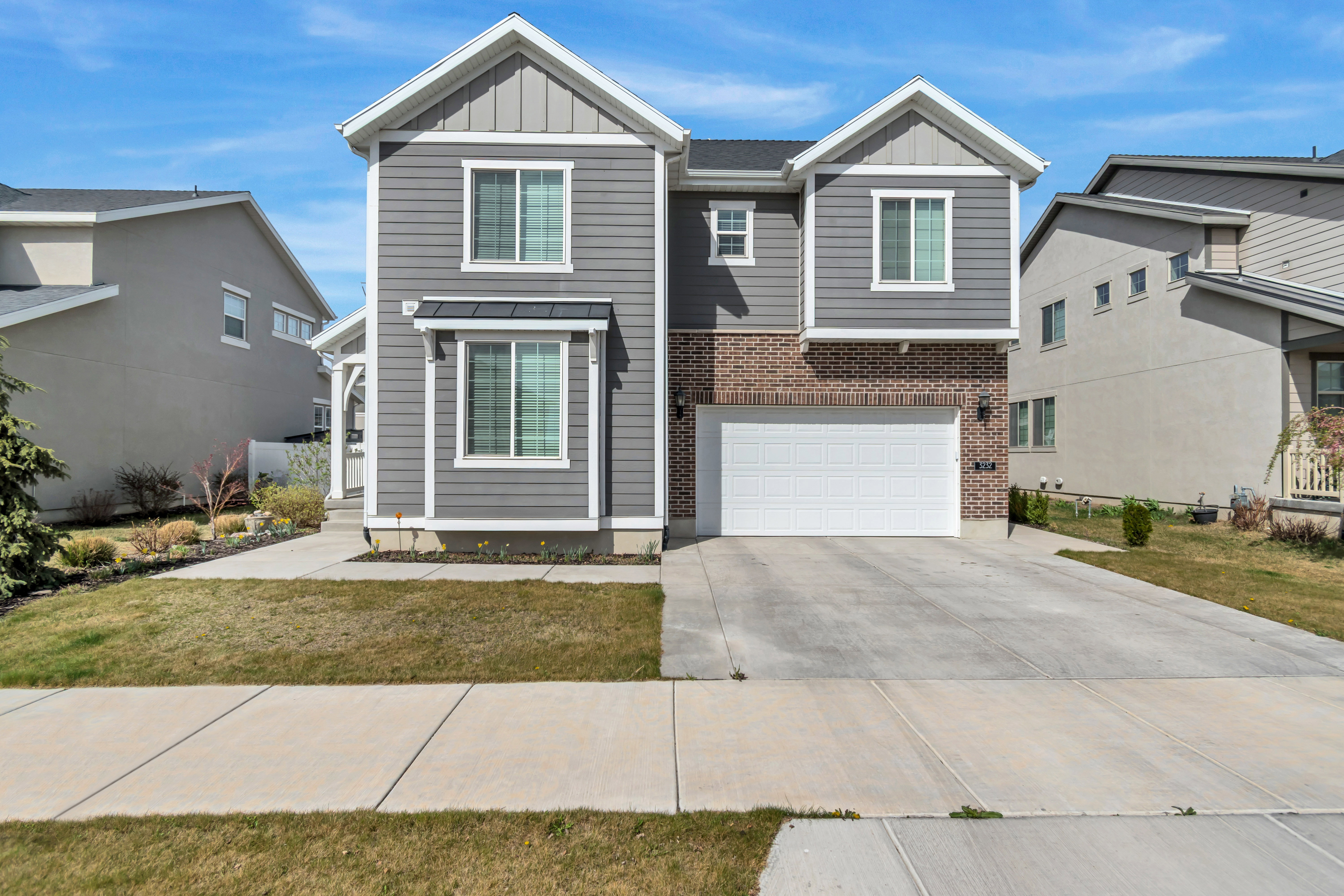 View of front of home with board and batten siding, driveway, a garage, and brick siding