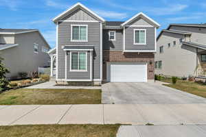 View of front of home with board and batten siding, driveway, a garage, and brick siding
