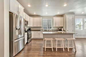 Kitchen featuring stainless steel appliances, white cabinetry, a breakfast bar, dark wood finished floors, and recessed lighting