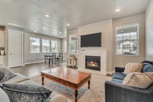 Living room with a glass covered fireplace, recessed lighting, light wood-style flooring, and a textured ceiling