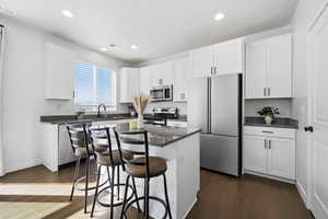 Kitchen with stainless steel appliances, a breakfast bar area, a center island, white cabinetry, and dark wood-type flooring