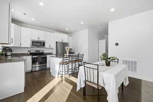 Kitchen featuring stainless steel appliances, white cabinetry, dark wood-style flooring, dark stone countertops, and recessed lighting