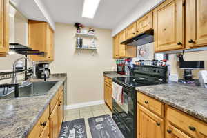 Kitchen featuring black range with electric cooktop, light tile patterned floors, open shelves, dark stone counters, and stainless steel dishwasher