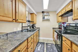 Kitchen with electric range, light tile patterned flooring, open shelves, dishwasher, and light wood finish cabinetry