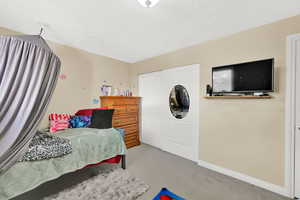 Bedroom with light colored carpet, a closet, and a textured ceiling