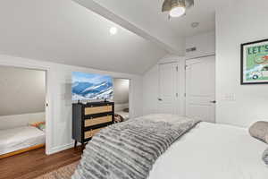 Bedroom with lofted ceiling, wood finished floors, and a textured wall