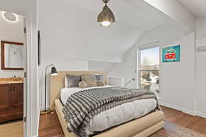 Bedroom featuring light wood-style floors, connected bathroom, and vaulted ceiling