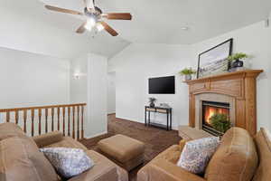 Living area featuring carpet, a ceiling fan, a fireplace, and vaulted ceiling