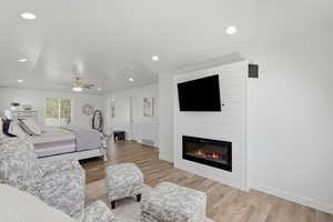 Bedroom featuring light wood-style floors, ceiling fan, a large fireplace, and recessed lighting
