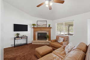 Living room featuring a brick fireplace, carpet, ceiling fan, and lofted ceiling