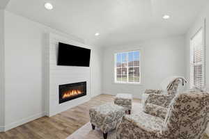Sitting room with light wood-style floors, a large fireplace, and recessed lighting