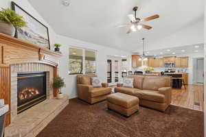 Living room featuring a brick fireplace, lofted ceiling, ceiling fan, recessed lighting, and carpet flooring