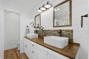 Bathroom with wood walls, double vanity, wood finished floors, and a wainscoted wall