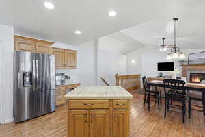 Kitchen with stainless steel refrigerator with ice dispenser, ceiling fan, a kitchen island, open floor plan, and a lit fireplace