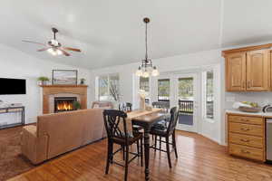 Dining area with light wood-style floors, ceiling fan, lofted ceiling, a fireplace, and hanging lights
