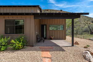 View of exterior entry with board and batten siding, a mountain view, and a patio area