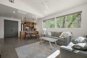 Living area featuring finished concrete flooring, vaulted ceiling, ceiling fan, and recessed lighting