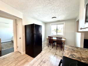 Kitchen with black appliances, light wood-type flooring, a textured ceiling, and dark stone counters