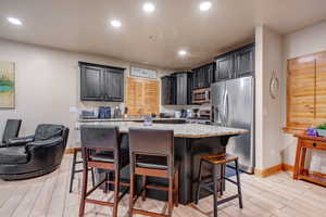 Kitchen with wood tiled floors, light stone counters, stainless steel appliances, a breakfast bar area, and a center island