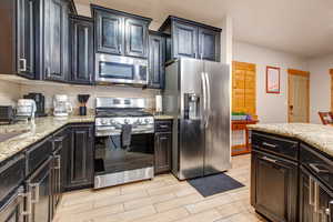 Kitchen with stainless steel appliances, wood tiled floors, light stone countertops, and dark cabinetry