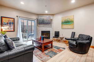 Living room featuring light wood-type flooring, a stone fireplace, and recessed lighting