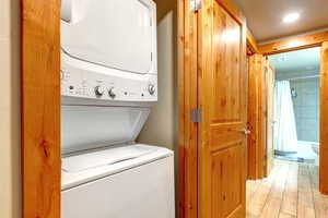 Laundry area with stacked washing machine and dryer, light wood finished floors, and recessed lighting