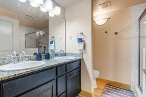 Full bath featuring double vanity, a stall shower, light wood finished floors, and a textured wall