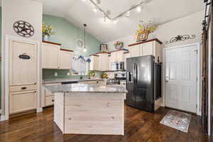 Kitchen featuring light stone countertops, stainless steel appliances, a center island, dark wood-style flooring, and a high ceiling