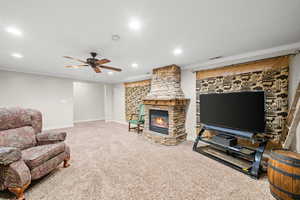 Living area with crown molding, light carpet, a ceiling fan, recessed lighting, and a stone fireplace