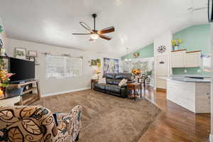 Living area with a ceiling fan, dark wood finished floors, healthy amount of natural light, a high textured ceiling, and a chandelier