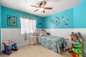 Bedroom with a wainscoted wall, a textured ceiling, a ceiling fan, and carpet